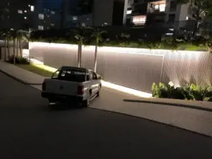 Detalhe de uma maquete noturna com iluminação externa e um veículo em frente a uma entrada de condomínio.