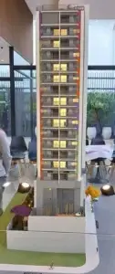 Maquete de edifício residencial alto, com varandas coloridas e iluminação interna, exibida em ambiente interno.