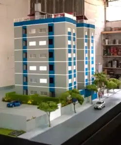 Maquete de edifício residencial com detalhes de fachadas em azul e cinza, além de paisagismo urbano.